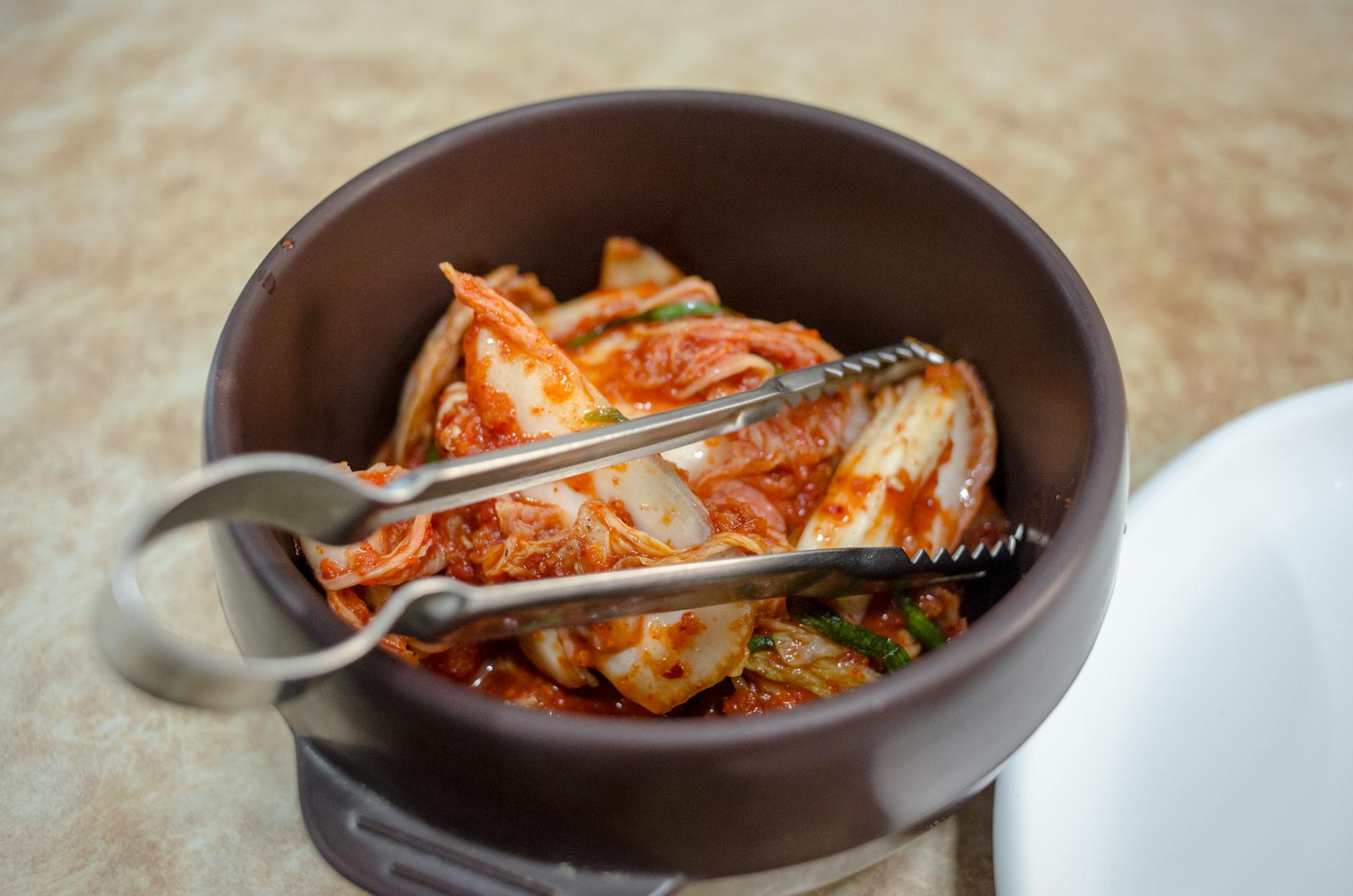 Pikantne koreańskie kimchi z ogórków w białej misce na drewnianym stole