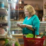 Starsza kobieta z koszykiem sprawdza listę zakupów w sklepie