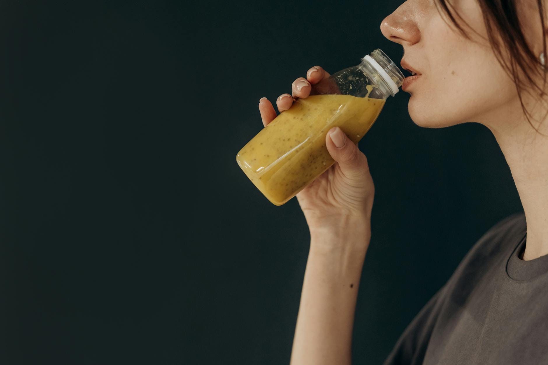 Młoda kobieta z profilu pijąca zdrowy koktajl z butelki