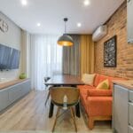 Nowoczesny salon w małym mieszkaniu z ceglaną ścianą i pomarańczową sofą