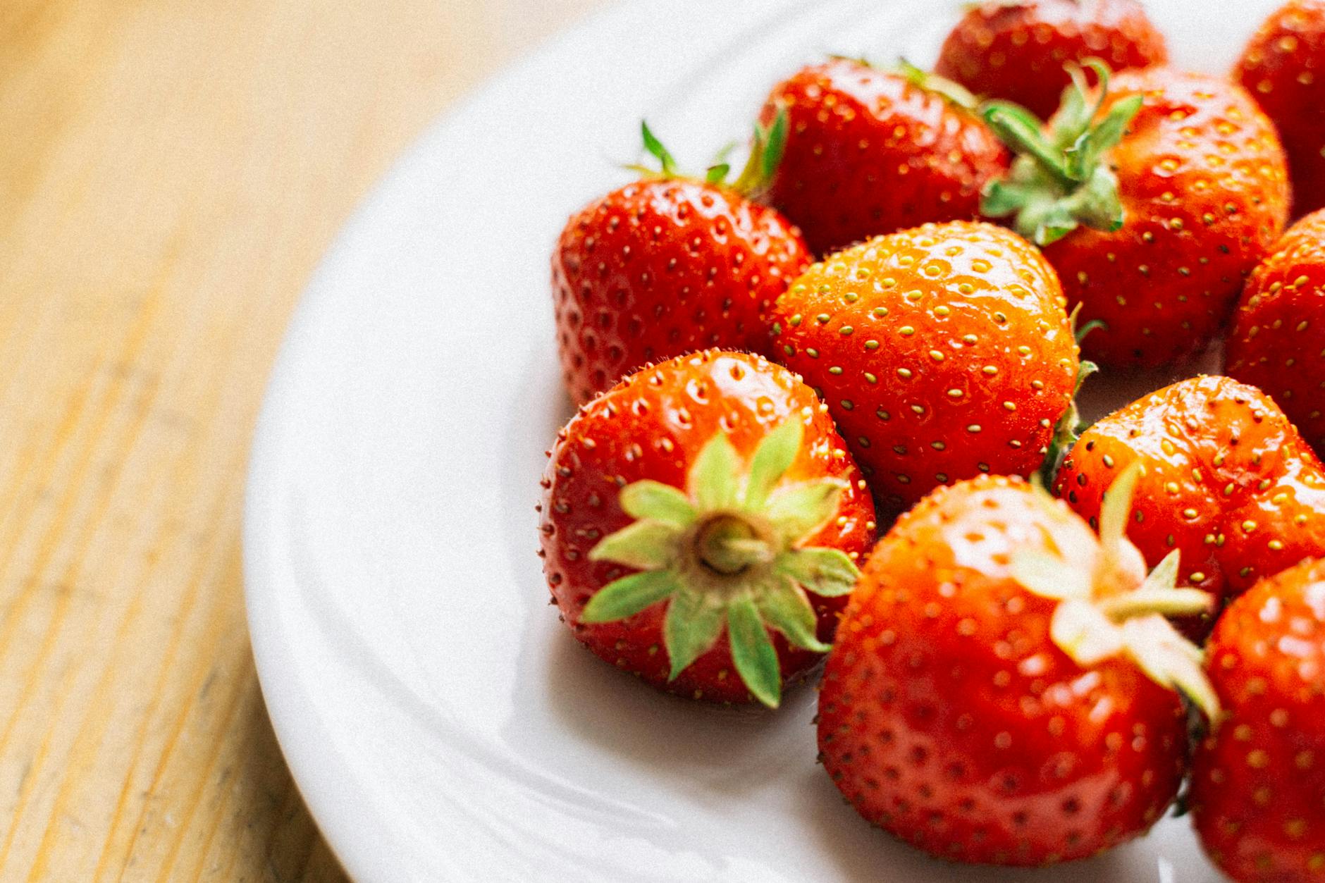 Świeże truskawki na białym talerzu na drewnianym tle