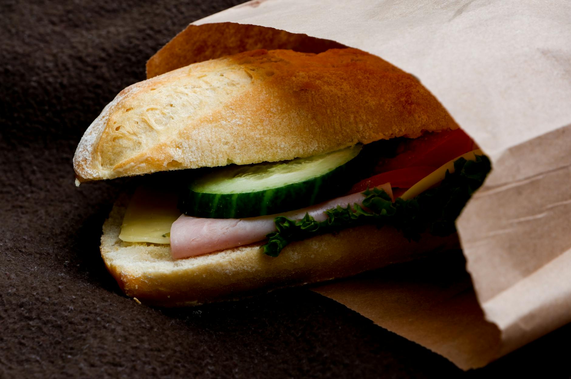 Kanapka z szynką, serem i warzywami w brązowej papierowej torebce