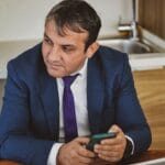 Biznesmen w niebieskim garniturze sprawdza dane firmy na smartfonie