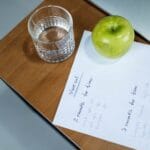 Zielone jabłko, szklanka wody i plan treningowy na drewnianym biurku
